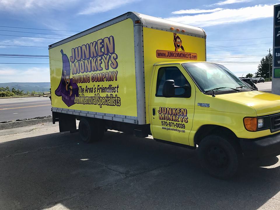 Yellow truck with "Junken Monkeys Hauling Company" and "The Area's Friendliest Junk Removal Specialists" written on it, parked near a road.