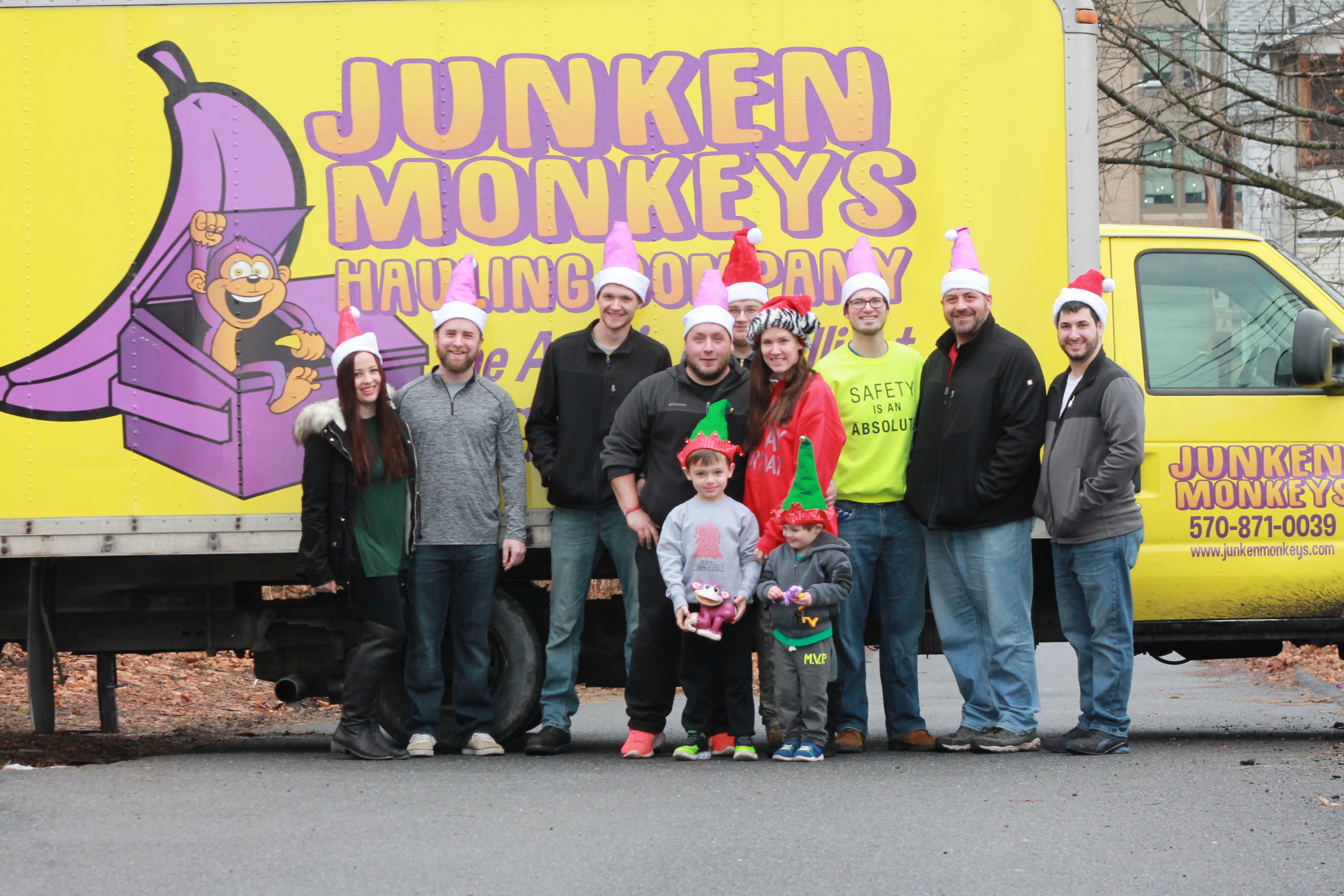 Group of people in festive hats standing in front of a yellow truck with "Junken Monkeys Hauling Company" written on it.