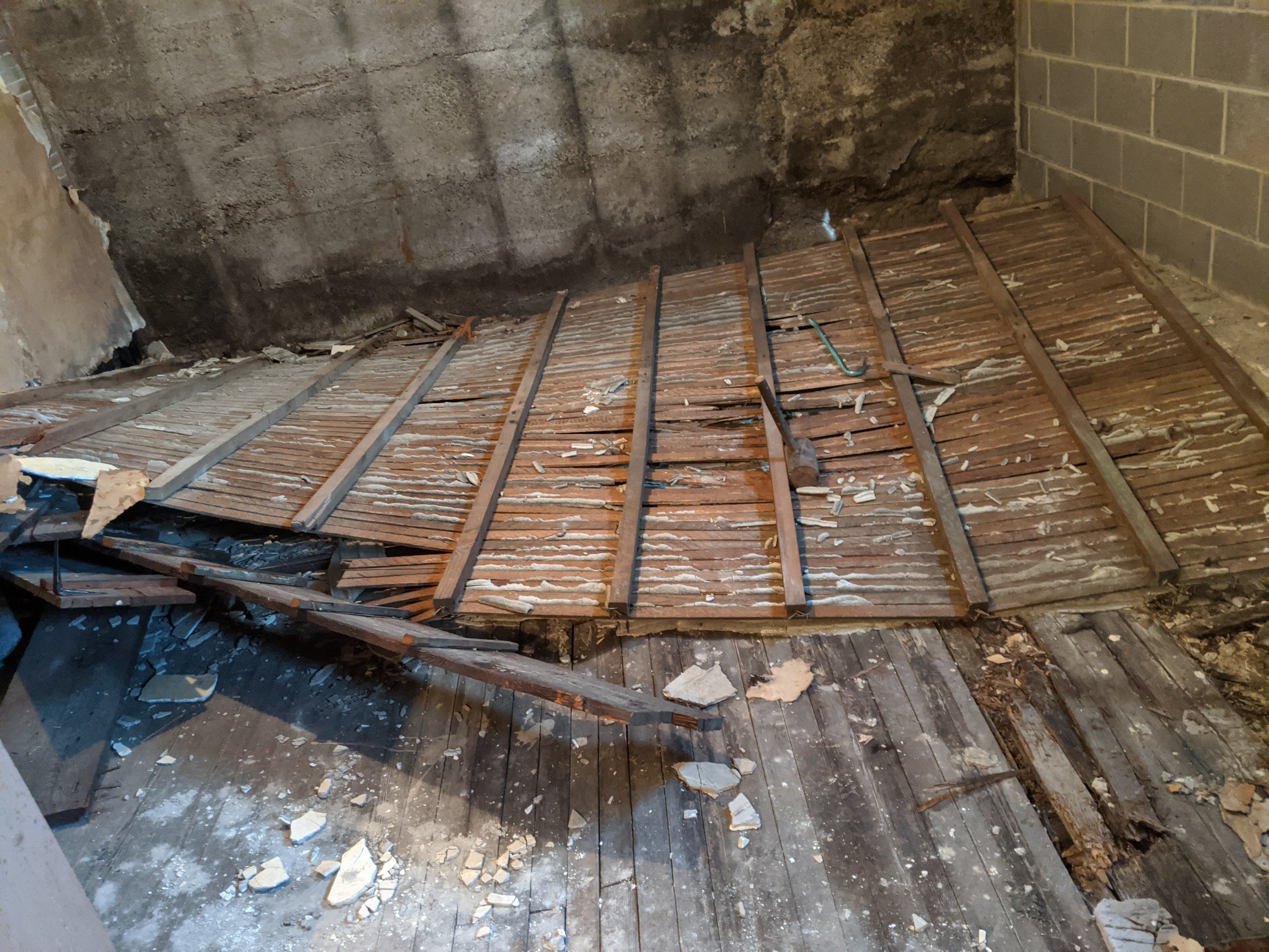 Collapsed wooden ceiling on a concrete floor in a dimly lit room with gray walls. Debris is scattered around.