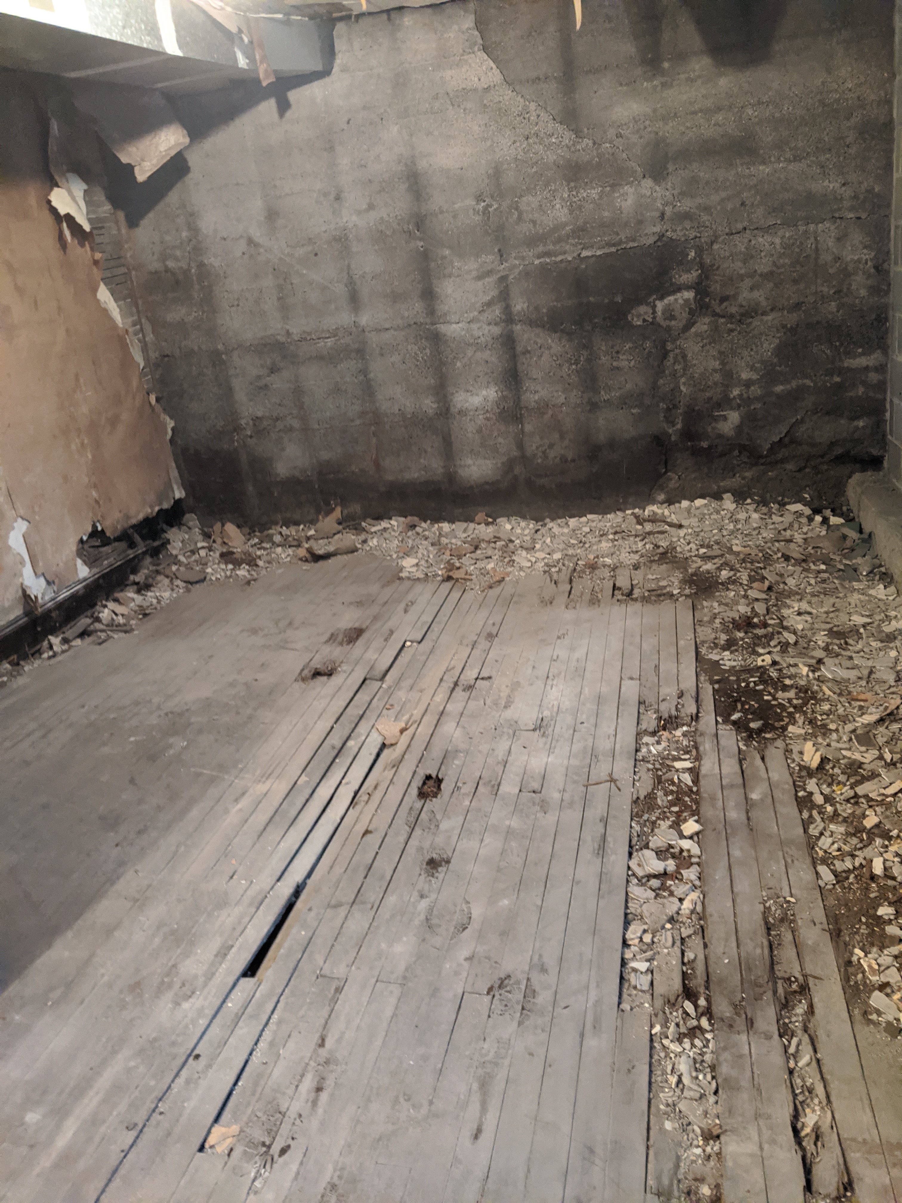 An empty, dilapidated room with peeling walls and a damaged wooden floor, surrounded by crumbling debris.