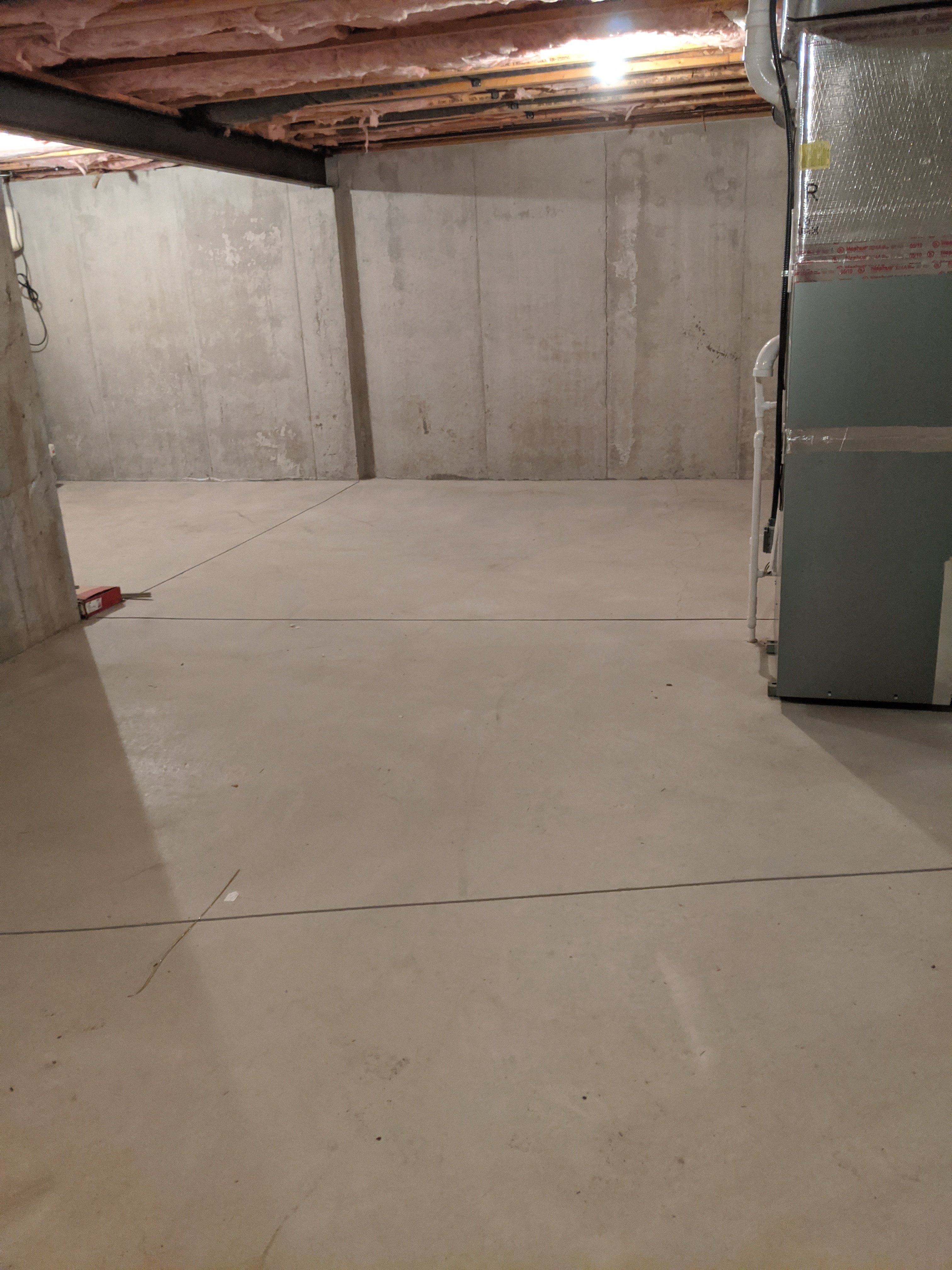 Empty basement with concrete walls and floor, exposed ceiling beams, and a furnace on the right.